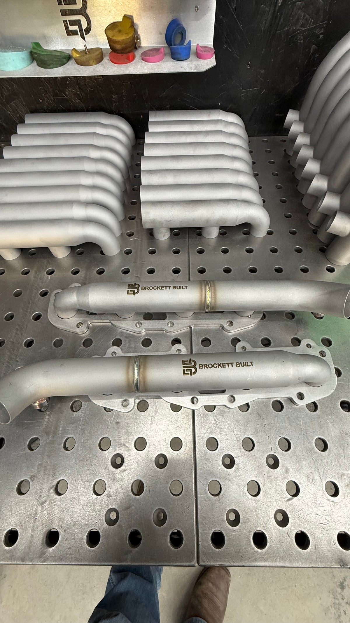 Brockett Built 3D printed 2UZ-FE shorty log manifolds, pair, 316L stainless, on the fixture table with more printed logs