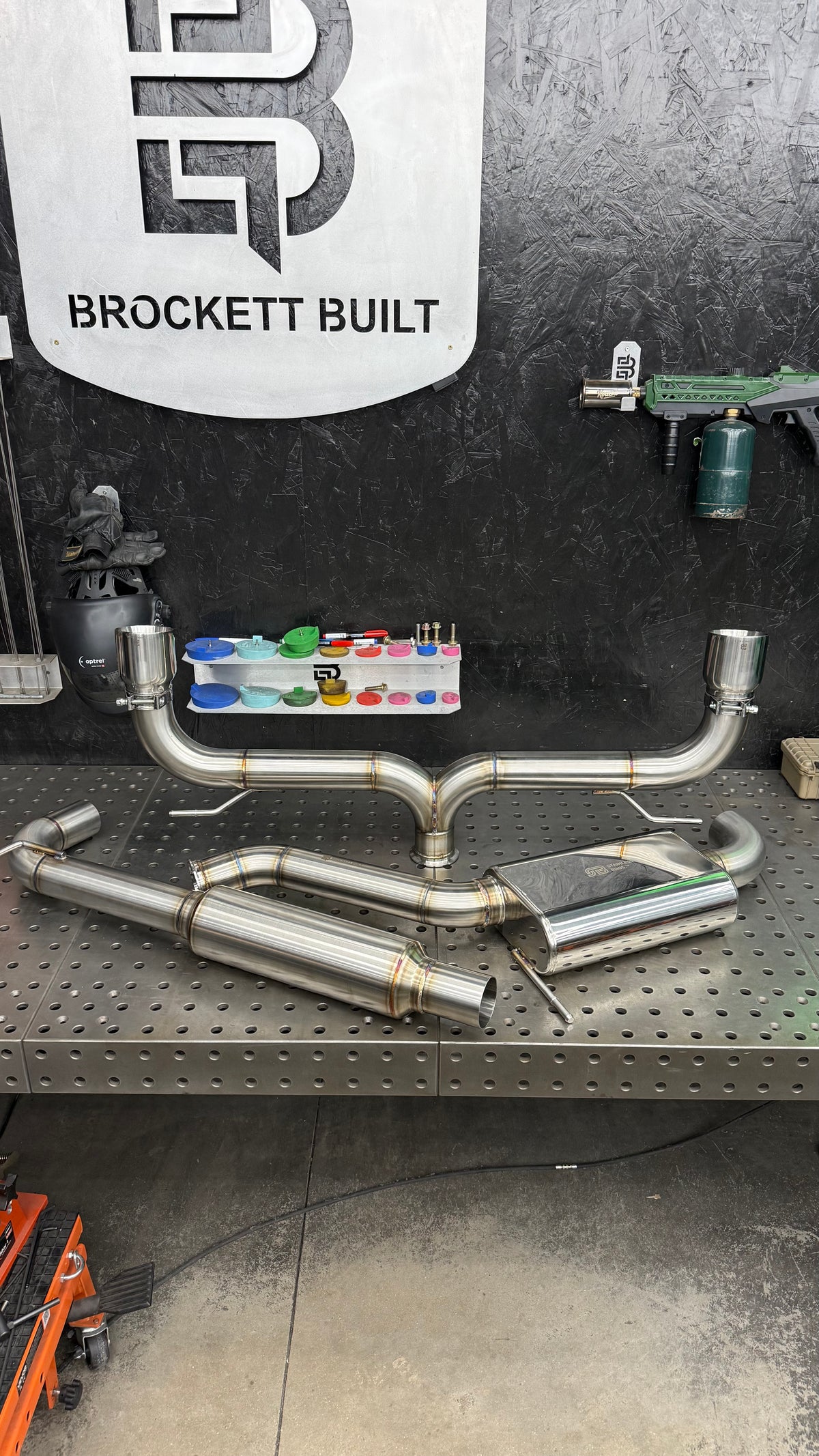 Brockett Built Aggressive cat-back exhaust for the Mk7 and Mk7.5 GTI on the fixture table under the shop sign, 3 inch dual exit with Jones tips and no rear muffler